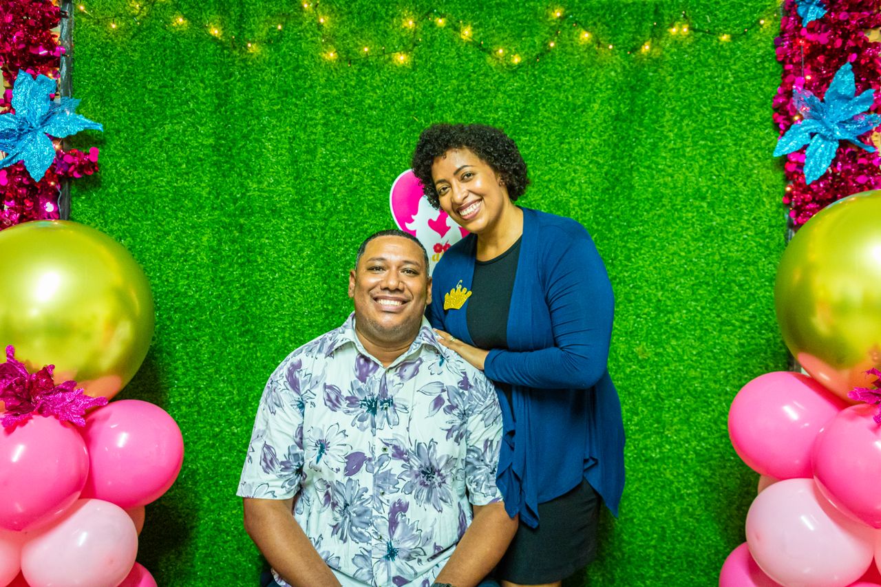 Lovely couple celebrating with colorful balloons and vibrant smiles against a green backdrop.