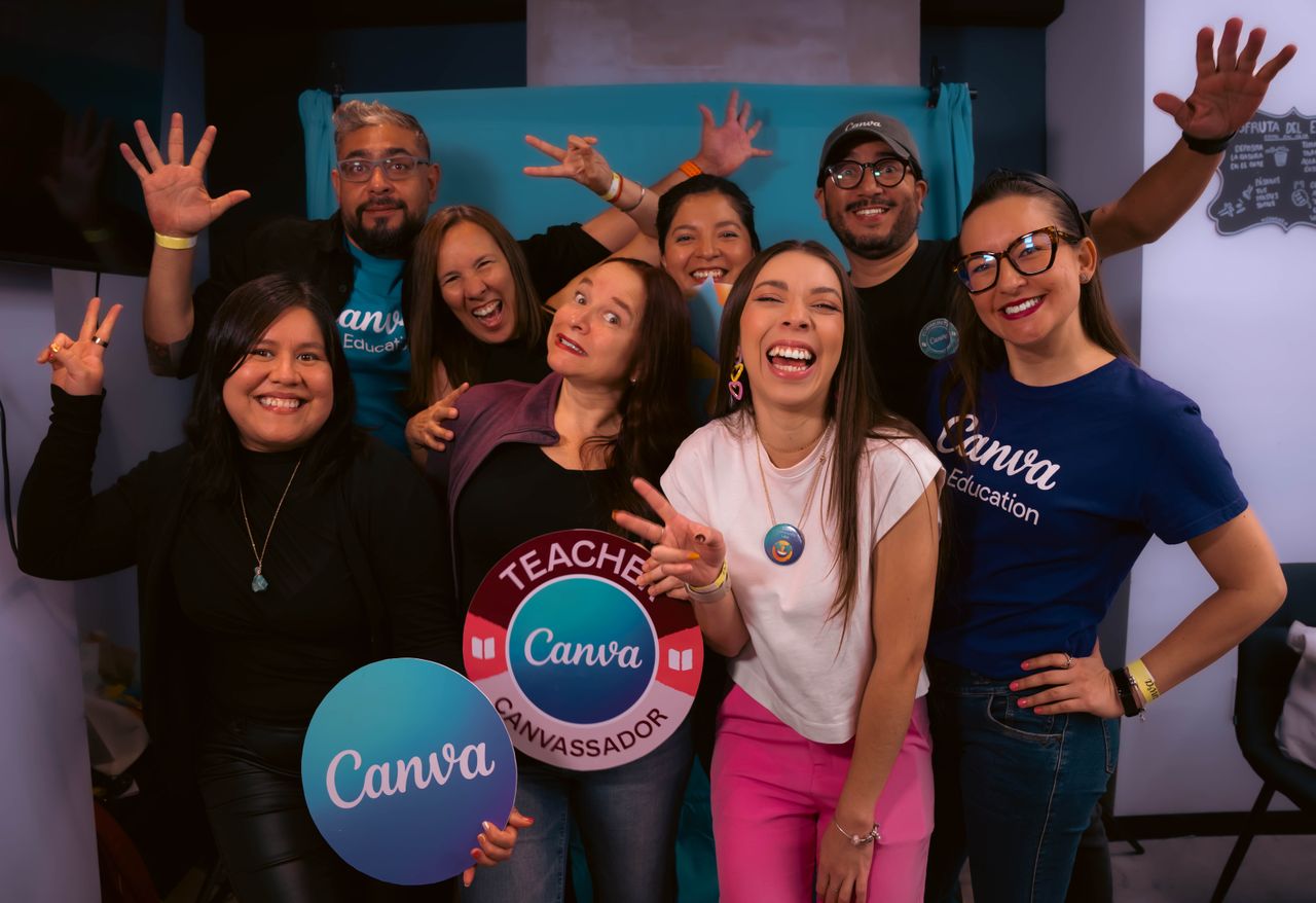 Group of adults joyfully posing with Canva signs at an indoor celebration.