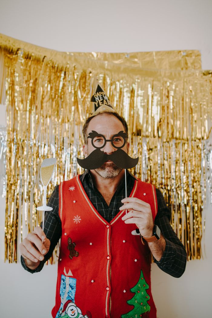 Man in festive attire celebrates New Year's with fun props and gold decorations.
